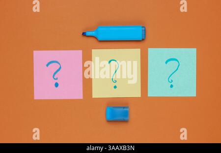 Memo pieces of paper with drawn question marks, felt-tip pen on brown background. Top view Stock Photo