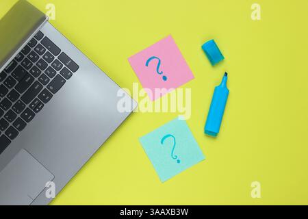 Laptop, memo pieces of paper with drawn question marks and felt-tip pen on green background. Top view Stock Photo