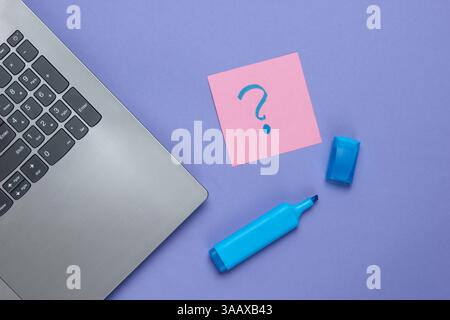 Laptop, memo piece of paper with drawn question marks and felt-tip pen on purple background. Top view Stock Photo