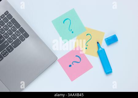 Laptop, memo pieces of paper with drawn question marks and felt-tip pen on white background. Top view Stock Photo