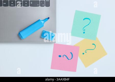 Laptop, memo pieces of paper with drawn question marks and felt-tip pen on white background. Top view Stock Photo