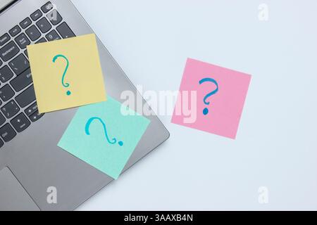 Laptop and memo pieces of paper with drawn question marks on white background. Top view Stock Photo