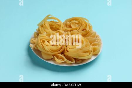 Different types of raw italian pasta in plate on blue background. Stock Photo