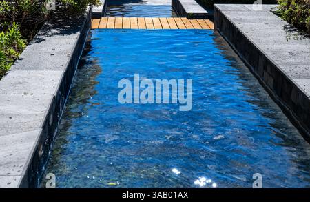 A small stream of water flows down a stone wall. The water is clear and calm, reflecting the sunlight Stock Photo