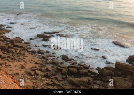 Soft ocean waves gently washing over rocks at sunset, creating a peaceful and serene coastal scene Stock Photo
