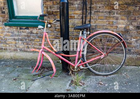 An old fashioned pink-painted bicycle chained to a lamp post in Islington, London, UK Stock Photo