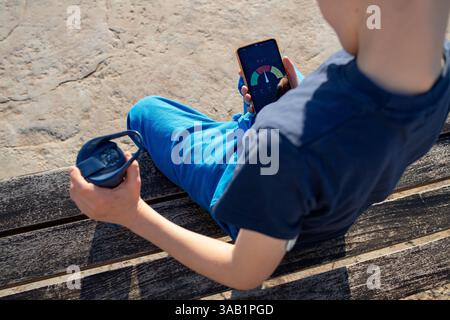Child with diabetes checks glucose app on phone, holding a water bottle. Stock Photo