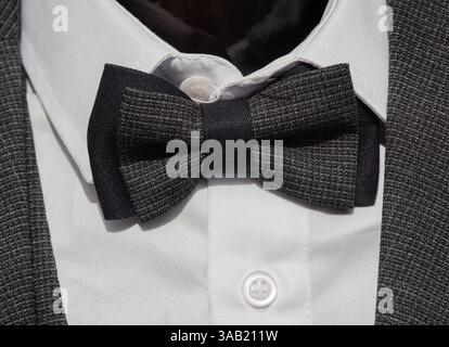 A close-up of a stylish black bow tie on a white shirt, complemented by a gray textured suit jacket. The bow tie features a subtle pattern, adding ele Stock Photo