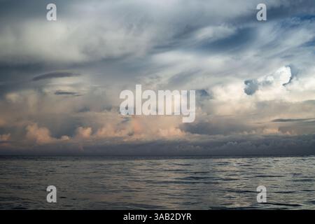 A tranquil ocean surface stretches beneath a dramatic cloudscape at dusk near Mauritius, with soft light and pastel colors reflecting on the water. Stock Photo