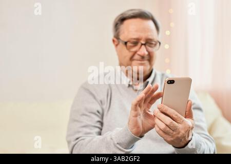 Senior man intently using his smartphone while sitting on a chair. Technology, communication, and senior lifestyle concept Stock Photo