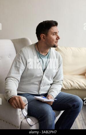 Portrait of handsome male psychologist and taking notes during therapy session at clinic. Friendly millennial psychotherapist posing and smiling at of Stock Photo