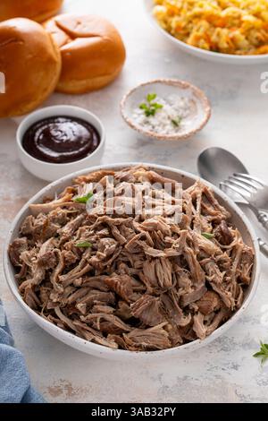 Pulled pork or carnitas cooked in a slow cooker served in a bowl to make sandwiches with brioche buns and cabbage Stock Photo