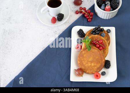 Delicious breakfast pancakes with assorted berries on a sleek white square plate over a diagonal blue cloth and gray background Stock Photo