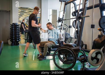 Caring sports coach aid athlete in wheelchair transfer after completing challenging training workout Stock Photo