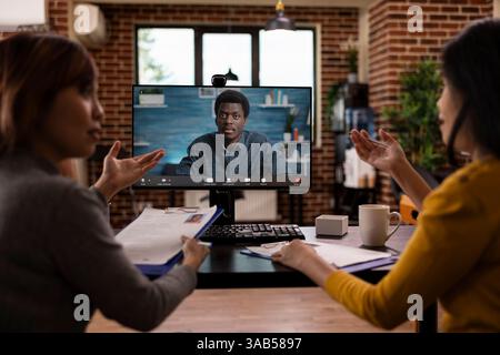 HR women staff discussing application forms with remote black manager on video call through computer. Female recruiters with clipboards, reading cv resumes to corporate client during virtual meeting. Stock Photo