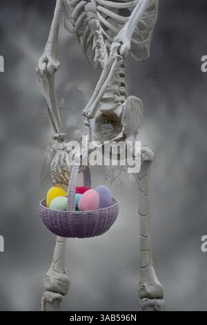 A human skeleton holds a basket filled with colorful Easter eggs against a foggy, gray background, creating a surreal scene Stock Photo