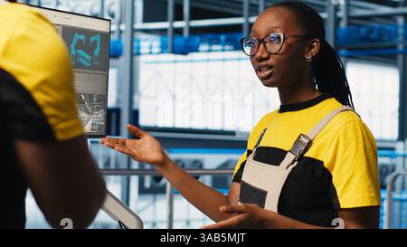 Engineering team in industry 4.0 industrial plant cooperating to install machinery, looking at monitor. Teamworking smart factory colleagues doing brainstorming to calibrate IoT sensors Stock Photo