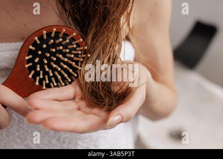 Woman brushing wet hair with wooden hairbrush after shower, close-up haircare routine, beauty and wellness, personal grooming, healthy hair concept. Stock Photo