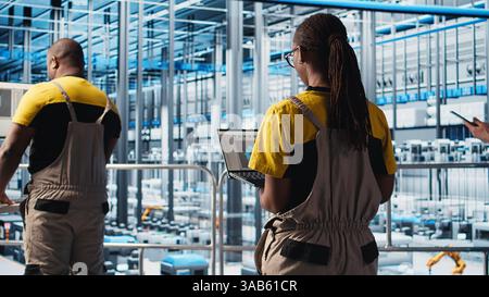 Engineering team working in smart factory, collecting and analyzing data. Teamworking colleagues using tracking software in industry 4.0 industrial plant equipped with advanced sensors, camera A Stock Photo