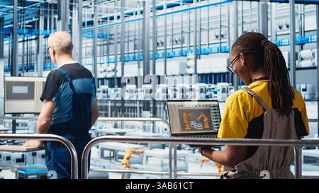 Engineers working in smart factory, collecting and analyzing data. Technicians using tracking software in industry 4.0 industrial plant equipped with advanced sensors, camera A Stock Photo