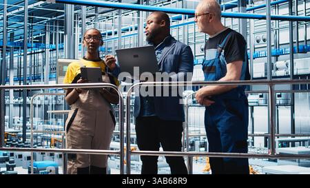 Smart factory manager teaching staff members to manage robotic arms using notebook. Supervisor overseeing industry 4.0 industrial plant, controlling automated machinery laptop, camera A Stock Photo