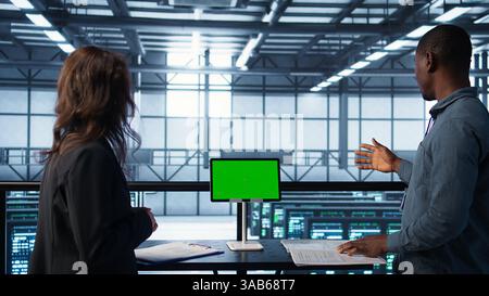 Data center team using mockup green screen tablet, reviewing paperwork files, and security protocols. Server room admins next to chroma key device analyzing critical system reports, camera B Stock Photo