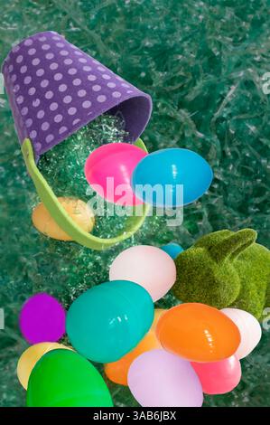 Easter pail basket full of plastic colorful eggs looks like all are falling on the grass with a green fuzzy easter bunny.. Lot of colors & polkadots. Stock Photo