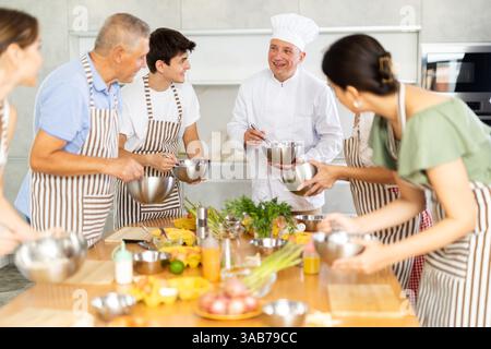 Cheerful middle-aged man chef of cooking course teaching attendees how to mix sauce Stock Photo