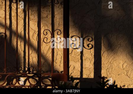 Ornamental gate casting shadows on textured wall Stock Photo