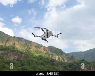 Drone hovering over blue sky and mountains. Quadcopter or drone hovering in bright blue sky Stock Photo