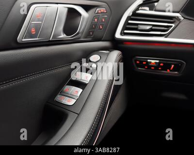 Door handle with power window control buttons. Black perforated leather interior with stitching. Modern car black leather interior details. Stock Photo