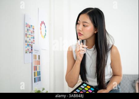 An asian woman is looking closely at a printed color palettes or a printed color wheel on the wall. Interior Designer or Graphic Designer working in o Stock Photo