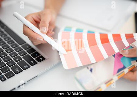 The hand holding a stylus pencil is choosing color from the printed color charts or color palettes. Interior Designer or Graphic Designer working in o Stock Photo