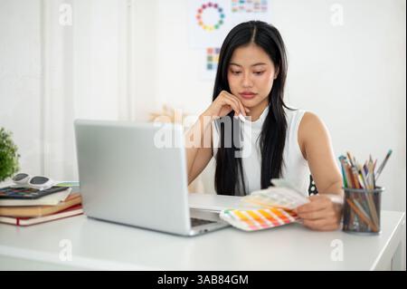 An asian woman is looking thoughtfully at the color charts or color palettes. Interior Designer or Graphic Designer working in office. Stock Photo