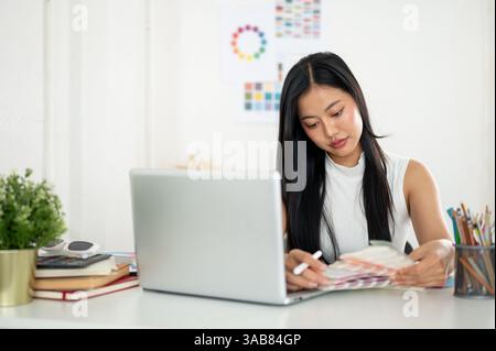 An asian woman is looking and choosing color from the printed color charts or color palettes in her hand. Interior Designer or Graphic Designer workin Stock Photo