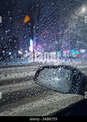Melting snow water drops on the car window with view to the outside mirror. Winter night urban scene Stock Photo