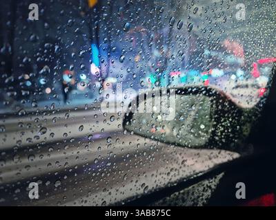 Melted snow and sleet drops on the car window with view to the side mirror. Winter night urban scene Stock Photo