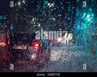 Winter night urban traffic scene as seen through the vehicle window covered with sleet drops. Melting snow water drips on the car windshield Stock Photo