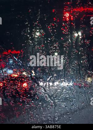Winter night urban traffic scene as seen through the vehicle windscreen covered with sleet drops. Melting snow water drops on the car window Stock Photo