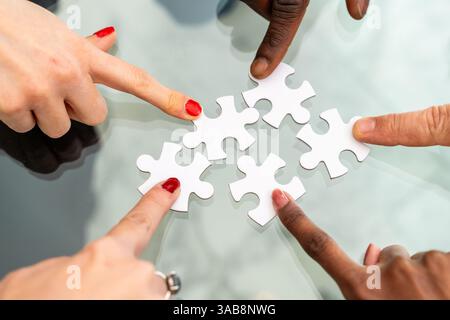 Hands of diverse businesspeople connecting puzzle pieces on glass table, symbolizing teamwork, collaboration, problem solving, inclusivity, and unity Stock Photo
