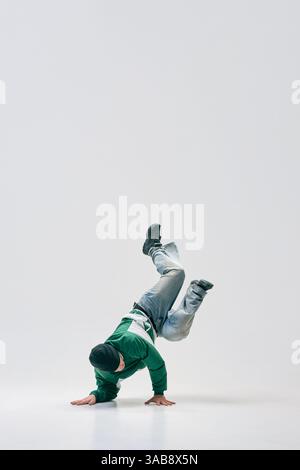 Breakdancer twisting mid-air while balancing on hands, showcasing flexibility and agility against white studio background. Stock Photo