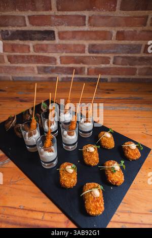 Elegant black slate platter featuring gourmet skewered appetizers in shot glasses with creamy dipping sauce, and crispy bite-sized snacks garnished wi Stock Photo