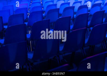A series of empty blue chairs are arranged in neat rows under a dramatic blue spotlight at a conference of AI in Amsterdam, creating a cool and contem Stock Photo