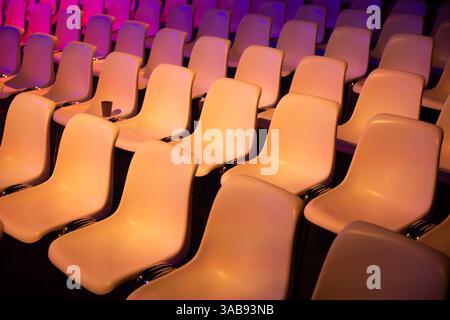 Rows of empty seats at a conference of AI in Amsterdam by vibrant purple and orange lights. The smooth curves and colors create a dynamic, inviting at Stock Photo