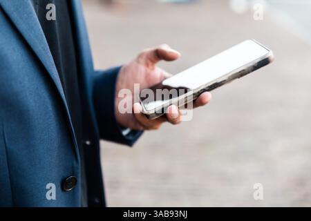 A indian man in a business suit checking their smartphone outdoors at a conference of AI in Amsterdam. The focus is on the hand holding the phone, sym Stock Photo