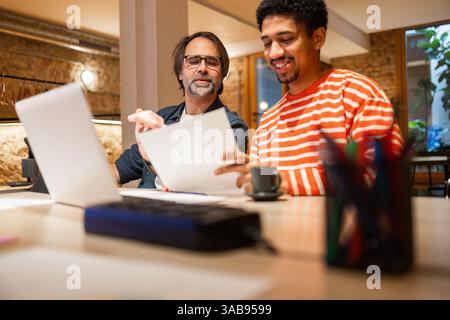 Two colleagues collaborating in a stylish coworking space, sharing ideas and working on a project together. Modern office environment with a casual, p Stock Photo
