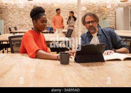 A diverse group of professionals collaborates at a modern coworking space They focus on shared tasks, promoting creativity and teamwork in a dynamic o Stock Photo