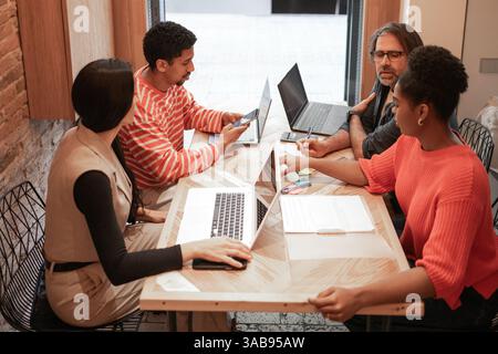 A group of diverse professionals collaborate in a modern coworking space, sharing ideas and working on laptops The setting promotes creativity and tea Stock Photo