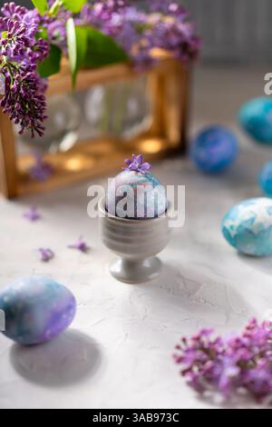Vibrant Easter eggs hand painted with galaxy patterns are displayed with delicate lilac flowers. Set on a textured surface, the scene evokes a sense o Stock Photo