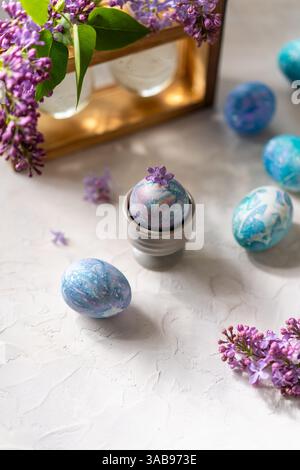 Vibrant, hand painted Easter eggs with marbled patterns surrounded by fresh lilac flowers, set on a textured surface. Perfect for a spring or Easter t Stock Photo